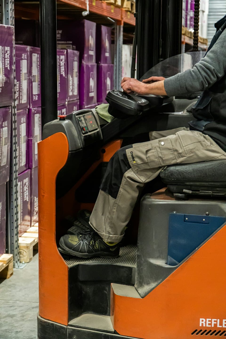 Worker operating a reach truck in a warehouse with purple boxes.
