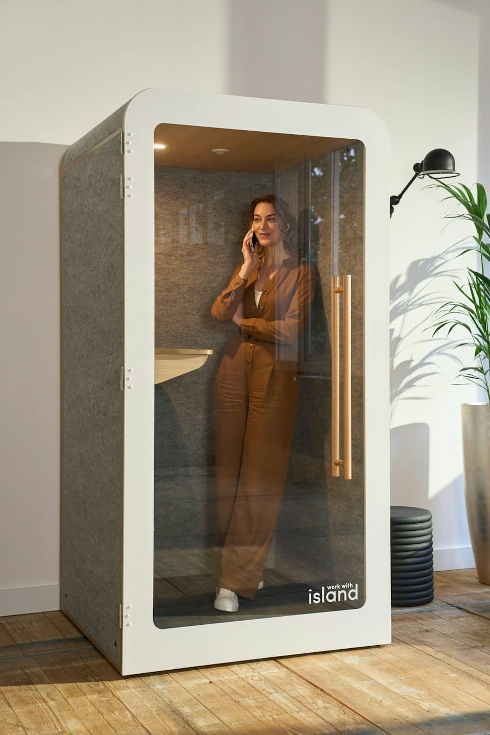 Woman in a brown jumpsuit talks on a phone inside a booth.